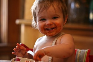 Un bebé riendo con la cara manchada de tomate mientras come