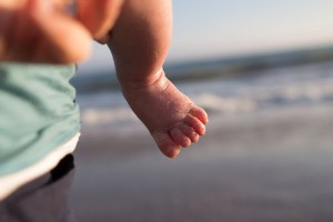 Pie descalzo de un bebé en la playa y en brazos de su mamá